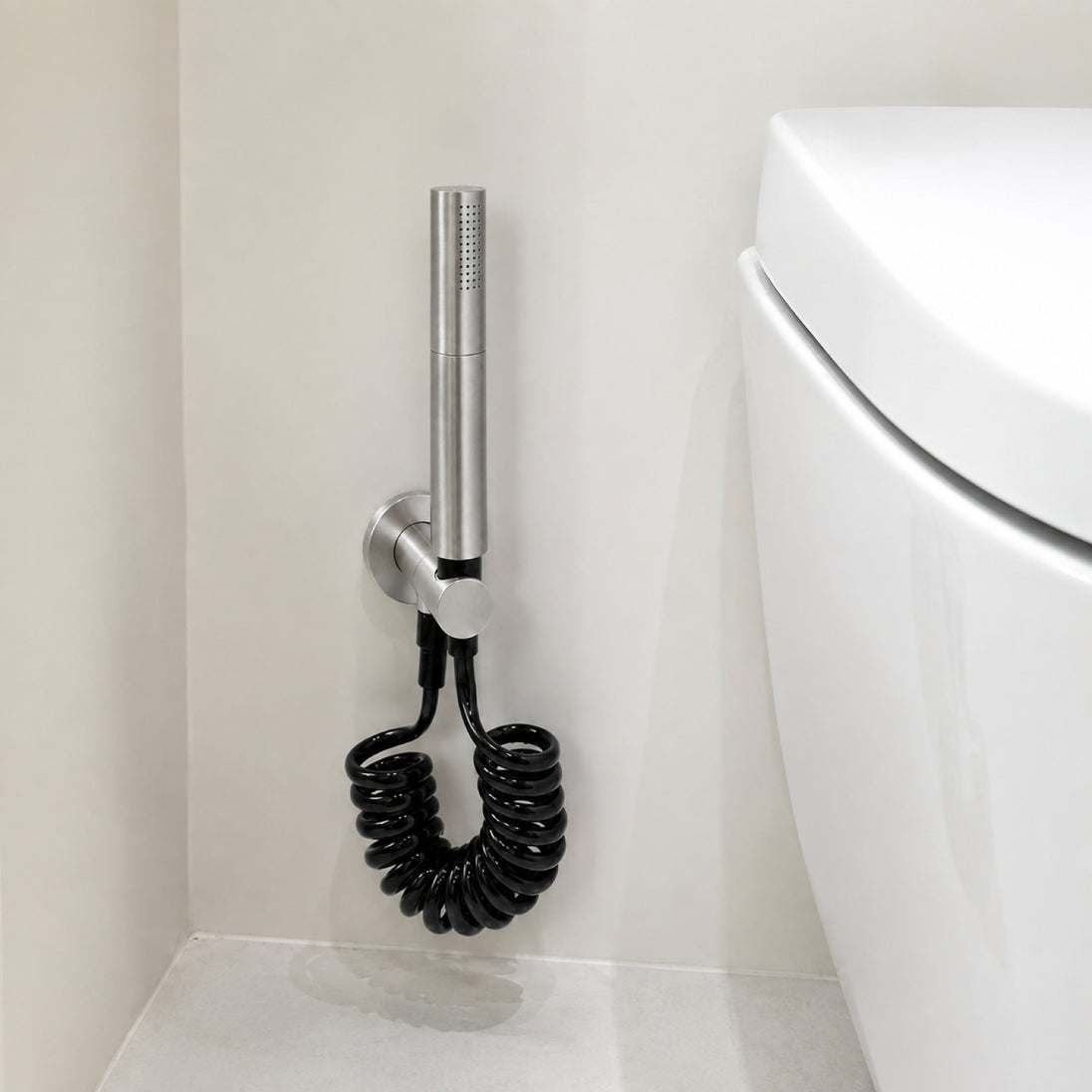 FILER rotary brass bidet sprayer with black coiled hose — installed bathroom scene